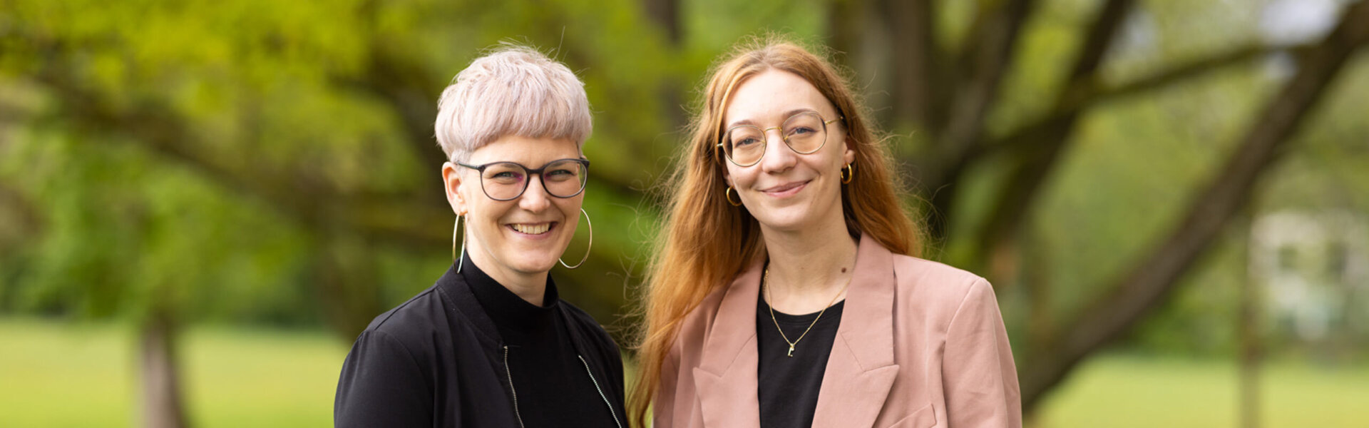 Die beiden Kolleginnen von MINT Salzburg stehen im Grünen und lächeln in die Kamera.