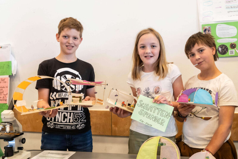 Drei Kinder präsentieren bei der MINT-Fair 2025 ihre selbstgebauten Modelle zum Thema Schattenspender.