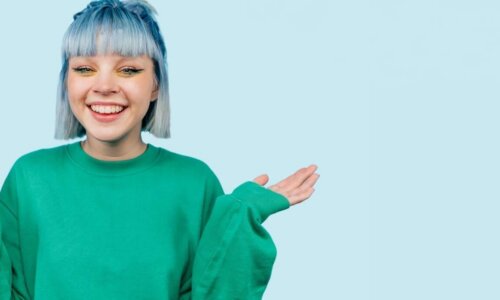 Ein Mädchen mit blauen Haaren lächelt breit und hebt beide Hände bis zur Schulter.