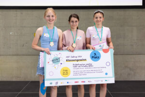 Drei Schülerinnen präsentieren bei der MINT Challenge 2026 ihren Preis für den dritten Platz auf der Bühne der BAUAkademie Salzburg.