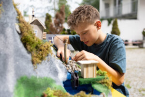 Ein Schüler arbeitet an einem Modell zur Nutzung von Wasserkraft mit Bachlauf und Wasserrad.