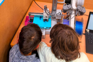 Zwei Kinder beobachten einen 3D-Drucker bei der Arbeit.