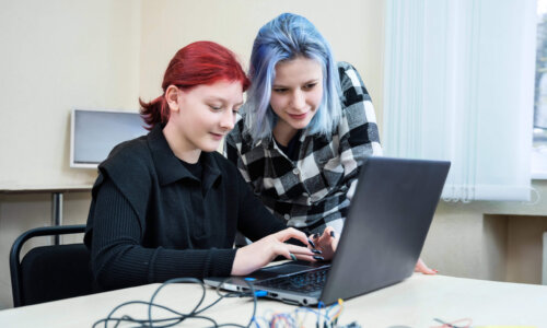 Zwei Schülerinnen arbeiten gemeinsam an einem Laptop und elektronischen Bauteilen in einem technischen Lernsetting.