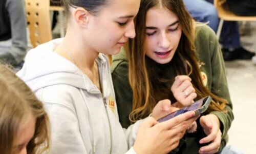 Zwei Schülerinnen betrachten gemeinsam ein Smartphone während einer Veranstaltung.